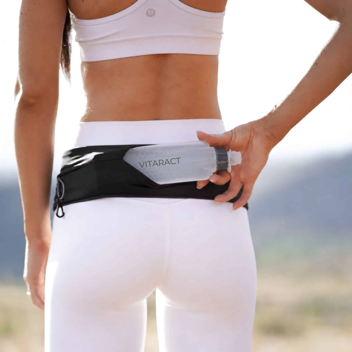 Runner outdoors pulling the Vitaract Arc water bottle from the back pocket of a black Vitaract running belt